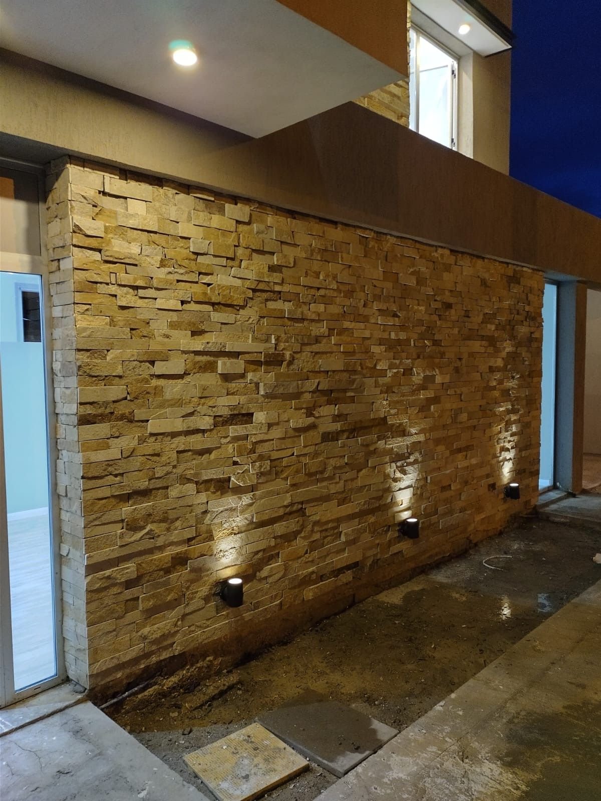 Muro de piedra iluminado en acceso de vivienda