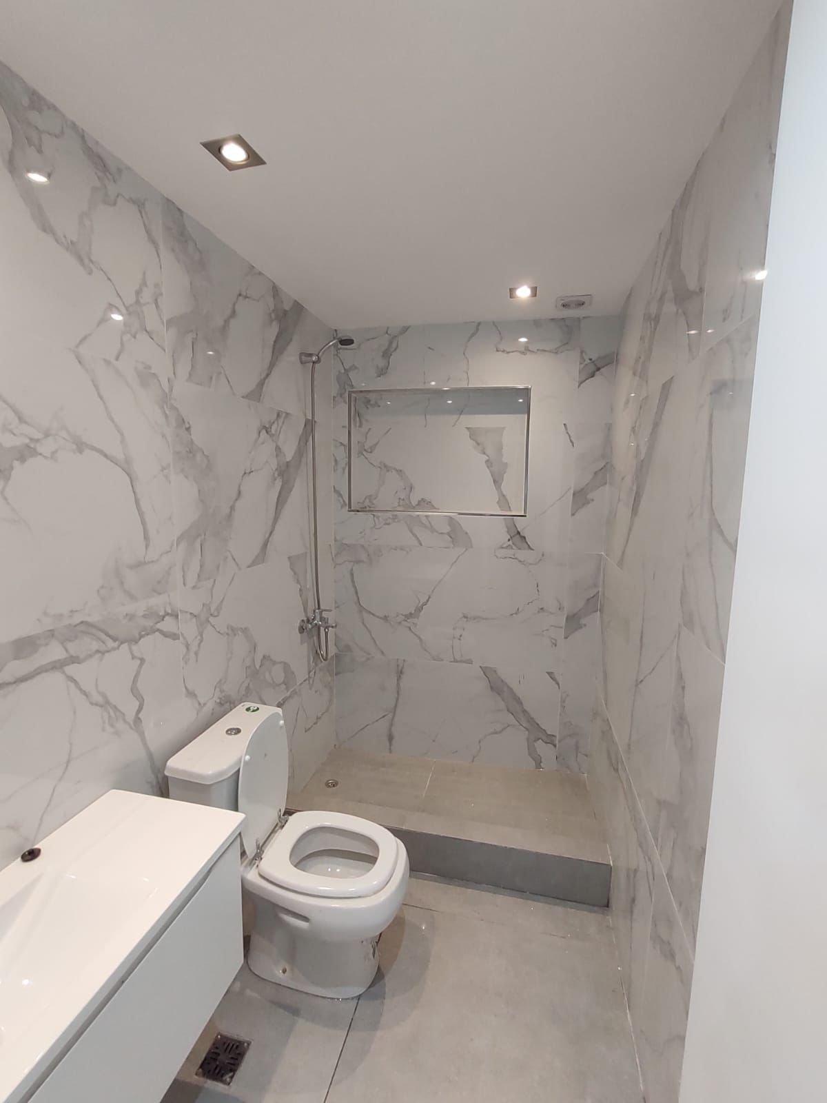 Baño terminado con revestimiento símil mármol y ducha con nicho